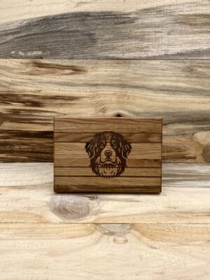 A handcrafted oak wood cutting board featuring an image of the face of a bernese mountain dog set against a wood backdrop.